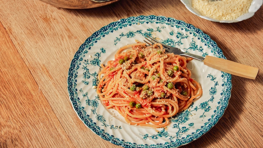 A plate of tomato, sausage and pea spaghetti topped with Parmesan cheese, a cheap and delicious weeknight pasta.