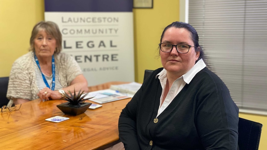 Two women sit at a desk in front of a sign for the Launceston Community Legal Centre.