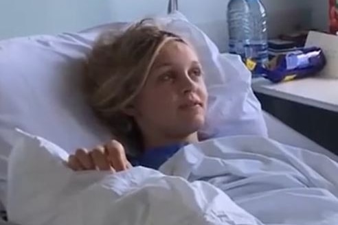 A young blonde woman lies on a hospital bed.
