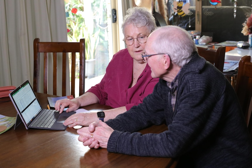 Man and woman sit at dining table talking in front of a laptop