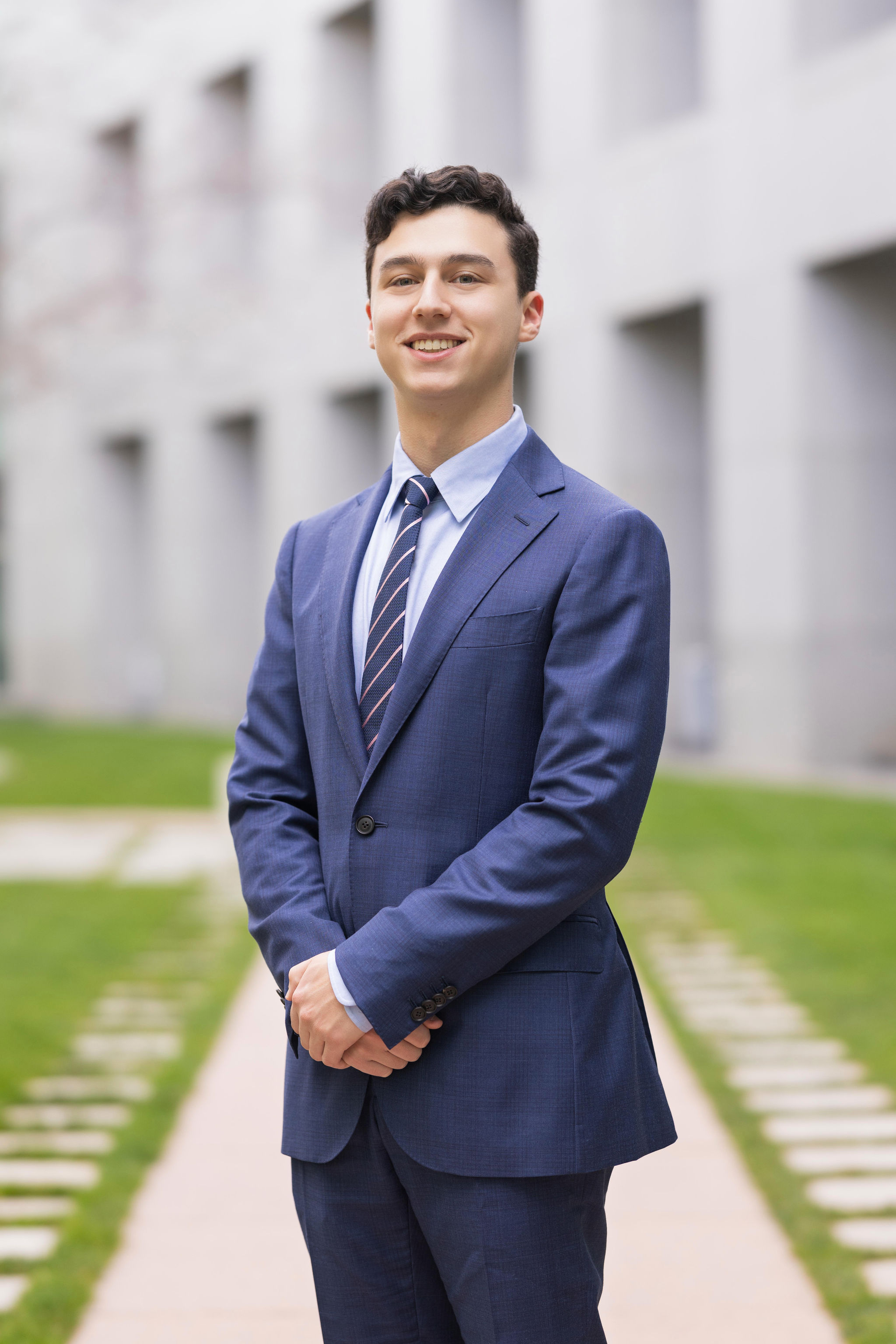 A young white man in a suit standing in a courtyard