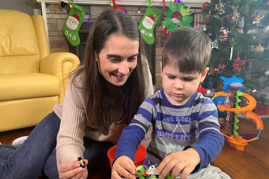 A woman smiles as she plays with a young boy and his toys.