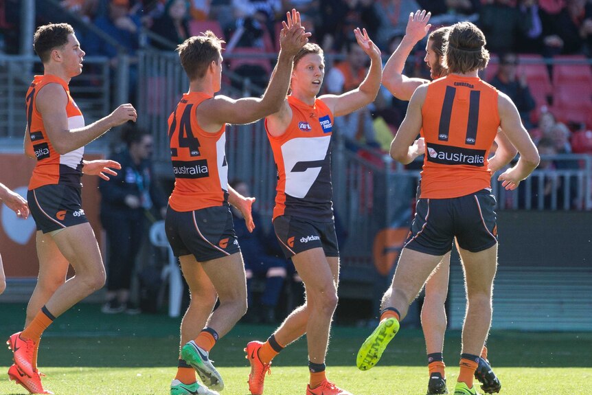 Three Giants players celebrate with Lachie Whitfield after he kicked a goal for GWS.
