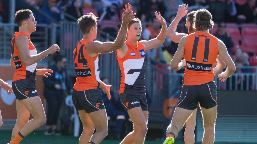 Three Giants players celebrate with Lachie Whitfield after he kicked a goal for GWS.