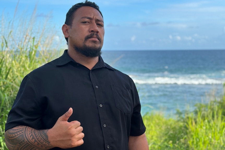 A photo of Tonga and Nuku'alofa resident Fononga Pulu, standing in front of the sea giving a thumbs up.