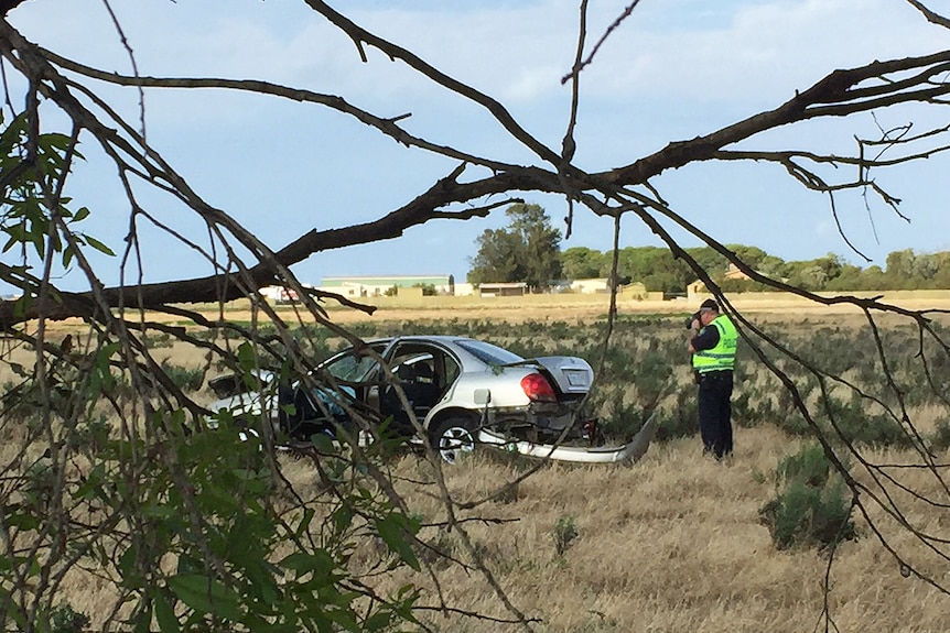 A policeman takes a photo of a crashed car in a field.
