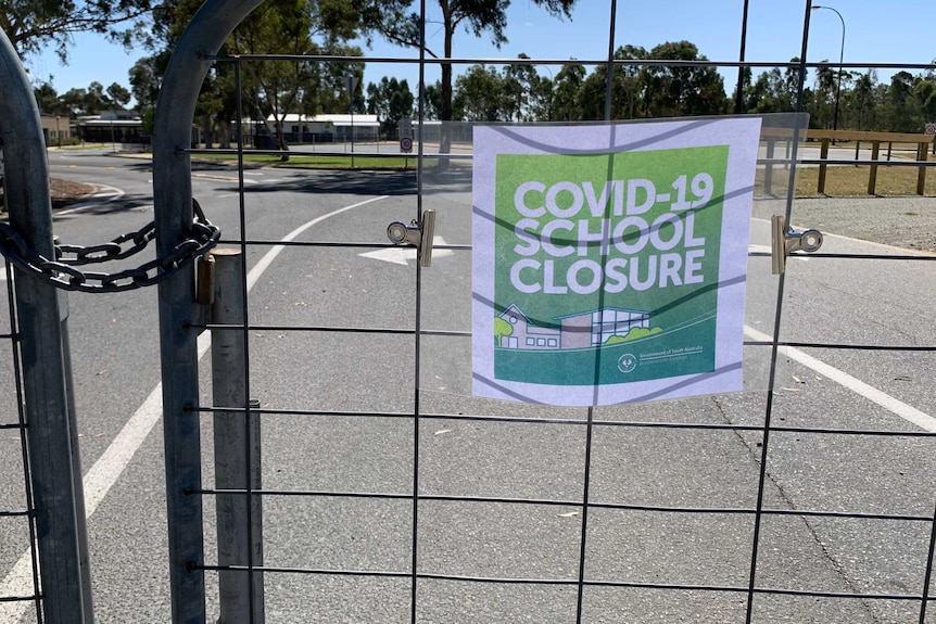 A sign reading 'COVID-19 school closure' on the closed gates of a school