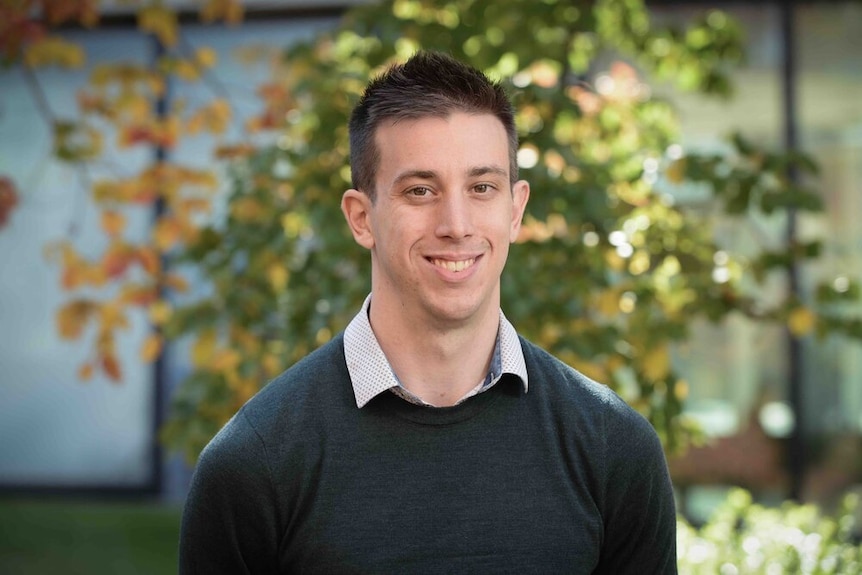 A headshot of a man in front of a tree.