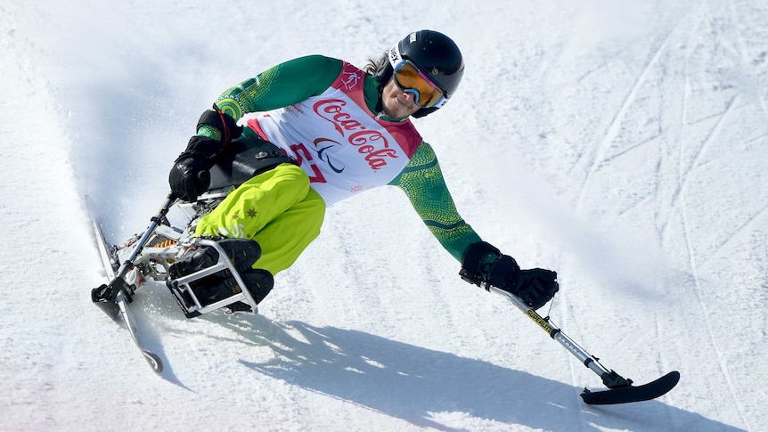 Sam Tait sits on a sit-ski and leans over stretching out one of his arms as he turns into a corner