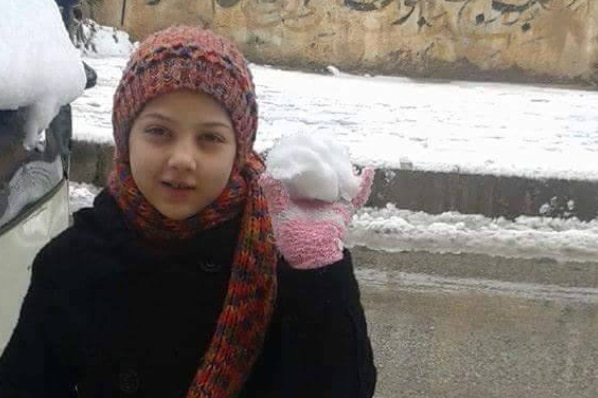 A girl wearing a black jacket holds up a snowball wearing pink mittens.