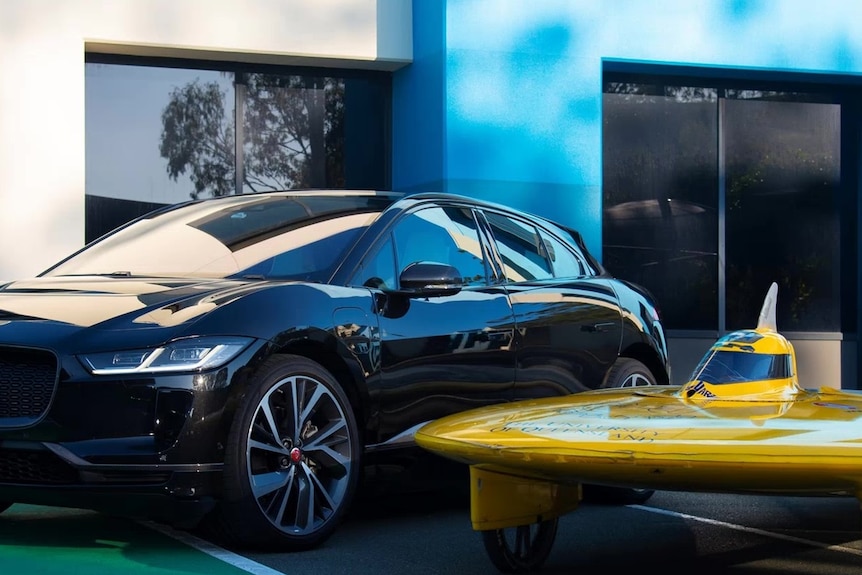 A very small and streamlined bright yellow car alongside a large black car