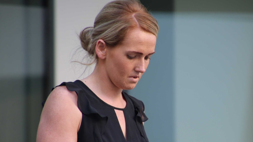 A woman wearing a black top looks down at the ground outside court.