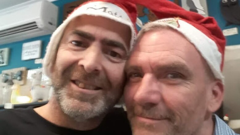 Two men pose for a selfie in Santa hats