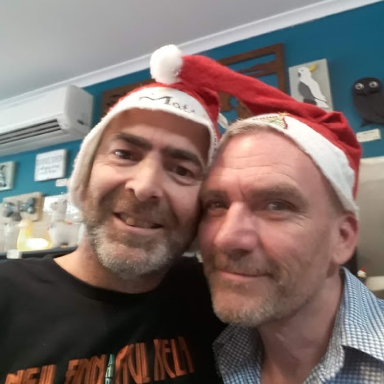 Two men pose for a selfie in Santa hats