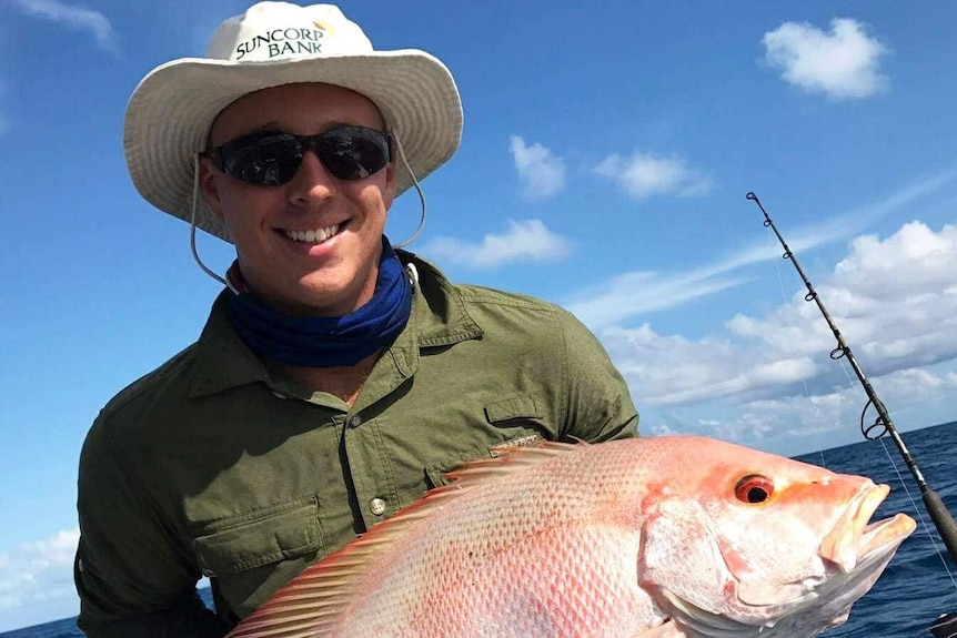 Jacob Bell on a boat holding a fish he has just caught