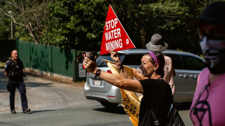 Protesters hold up signs that say 'Stop water mining' as police look on.