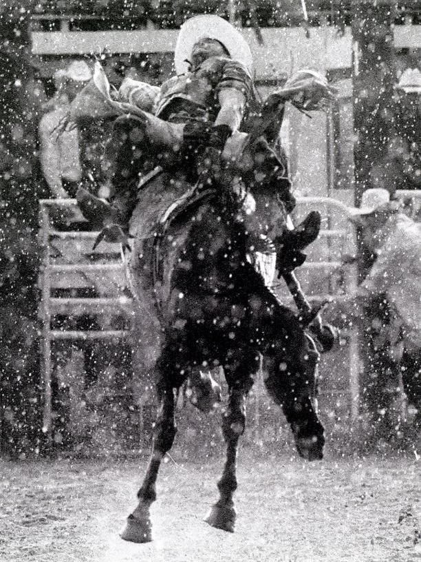 A man rides a bucking horse at a rodeo.