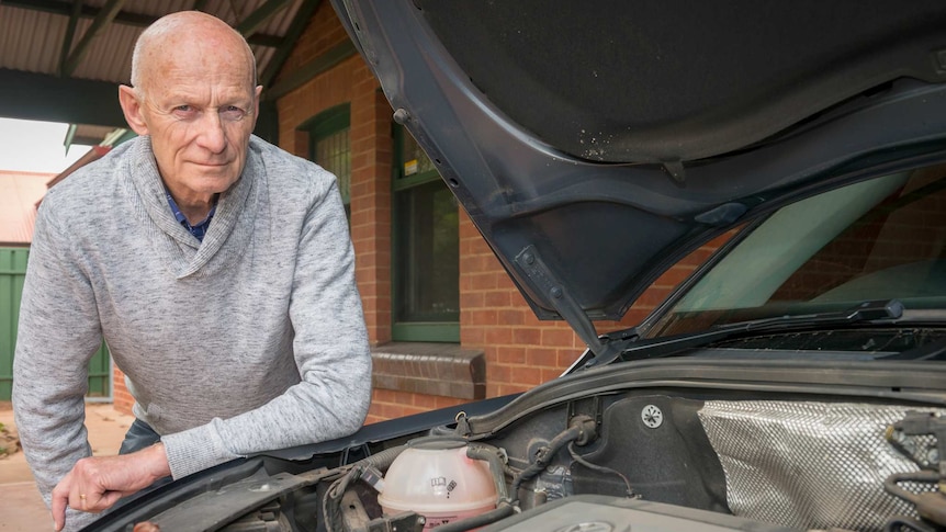 A man leans over the engine of his car.