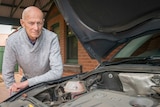 A man leans over the engine of his car.