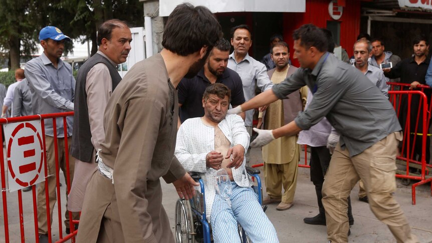 A group of men help to move an injured man in a wheelchair.
