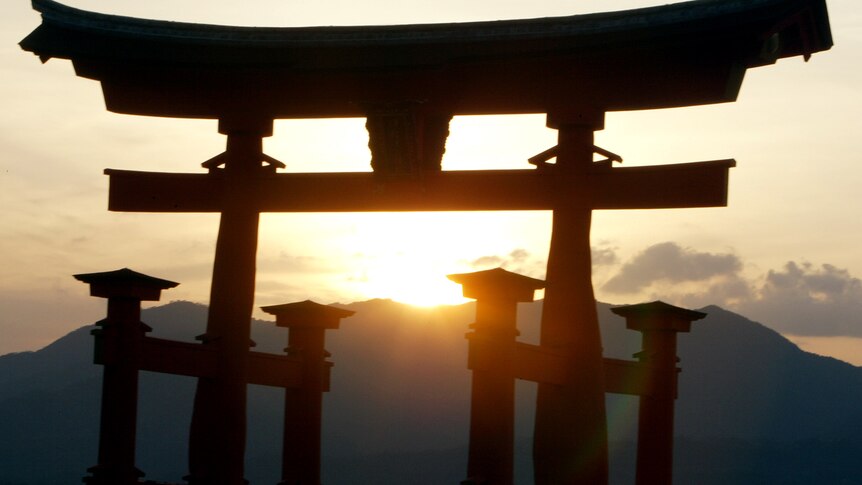 the sun sets over a mountain behind a torri gate in Miyajima
