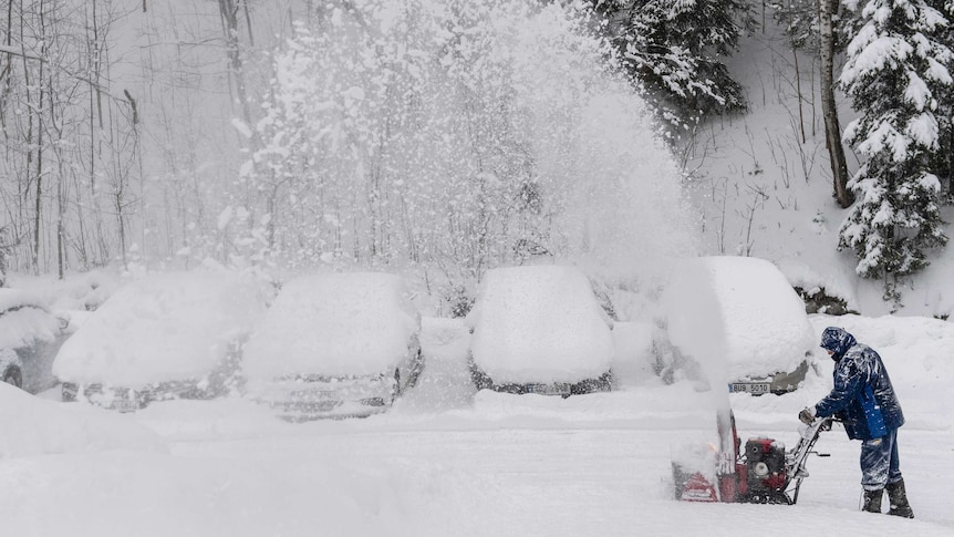 A man with a snow cutter cleans a road in heavy snowfall