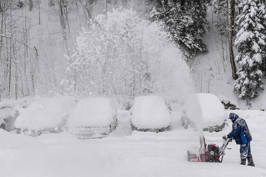 A man with a snow cutter cleans a road in heavy snowfall