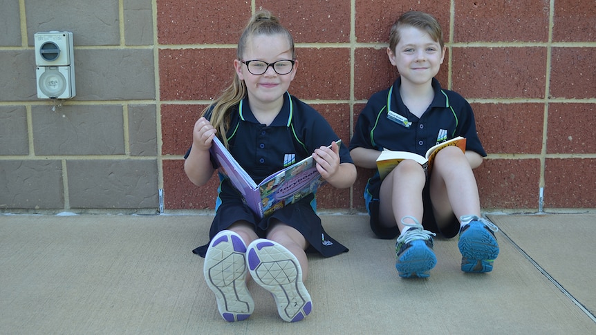 Colour photo of primary school students Ruby and Oliver sitting on ground reading books.