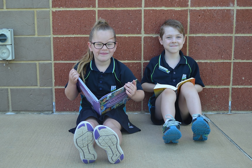 Colour photo of primary school students Ruby and Oliver sitting on ground reading books.