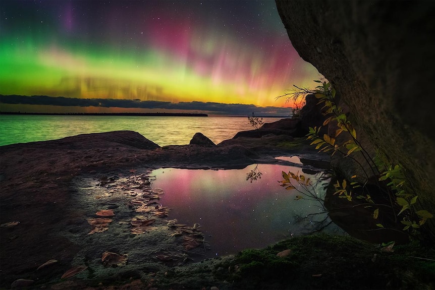 A green yellow and pink aurora behind a cove. 