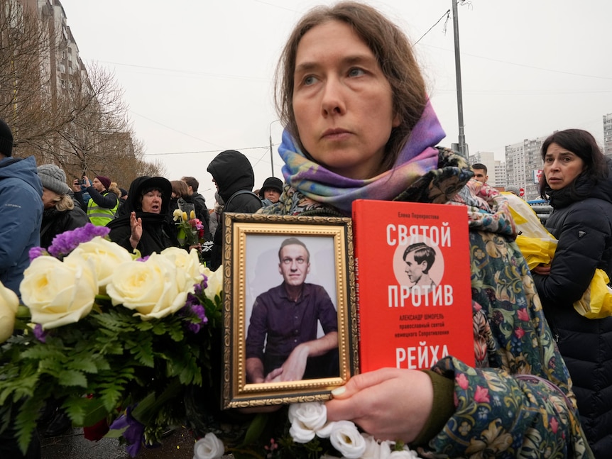 A woman holds a portrait of Alexei Navalny and a book titled "A saint against the Reich" 