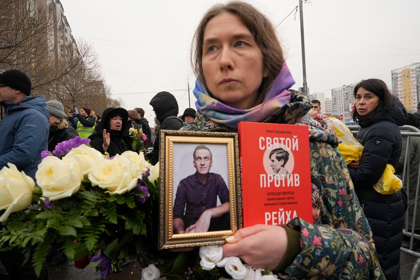 A woman holds a portrait of Alexei Navalny and a book titled "A saint against the Reich" 