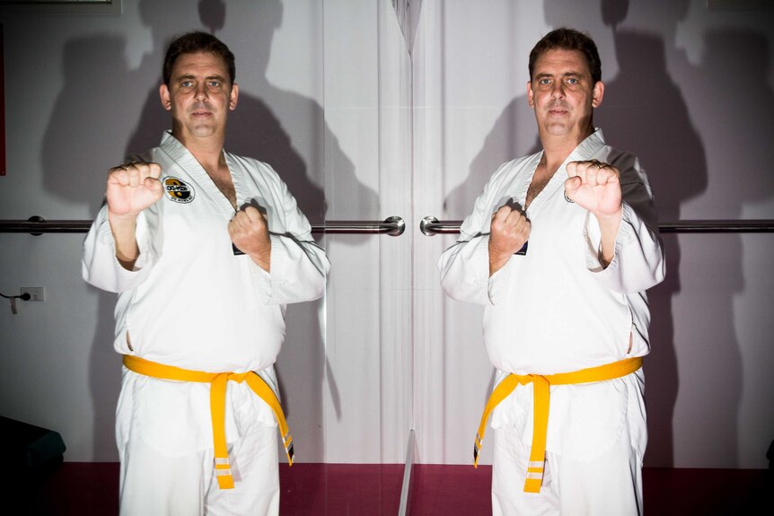 Adrian Hill stands next to a mirror in a taekwondo pose.