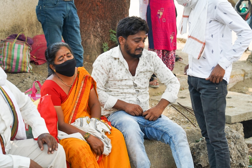 An Indian man and woman sitting outside, crying