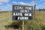 Black sign reading "coal mine here? save our farms" pitched into dry grassland