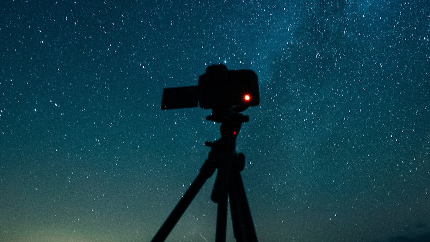 A camera is set up on a tripod in front of a blue and green night sky