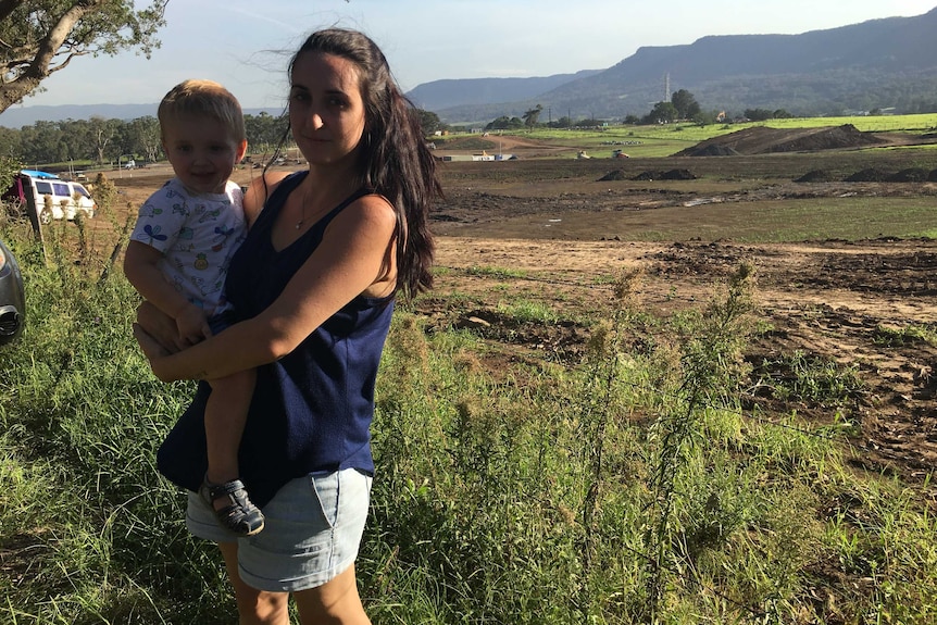 Kembla Grange resident Ami Beck stands at the site of the proposed prison in the Illawarra with her baby.
