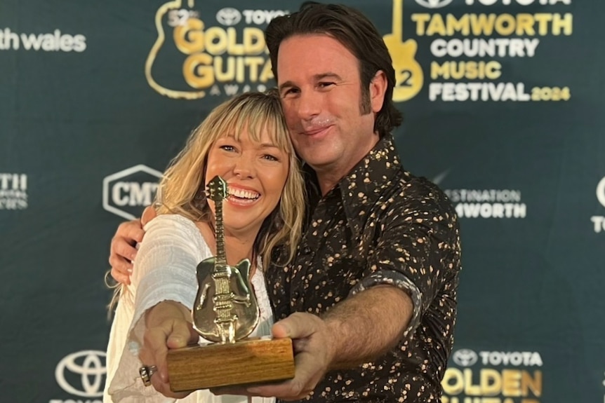 A man and a woman hug while holding a golden guitars