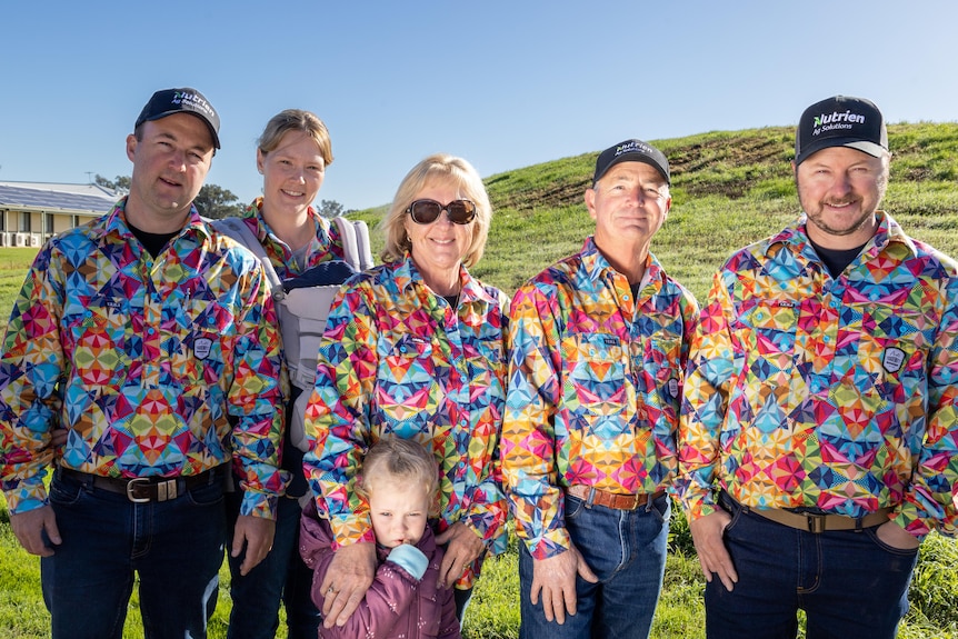 Five adults and a child stand side by side wearing rainbow shirts 