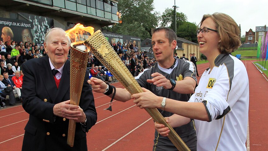 Firming in betting ... Sir Roger Bannister (L) passes the Olympic flame during the torch relay's journey around England