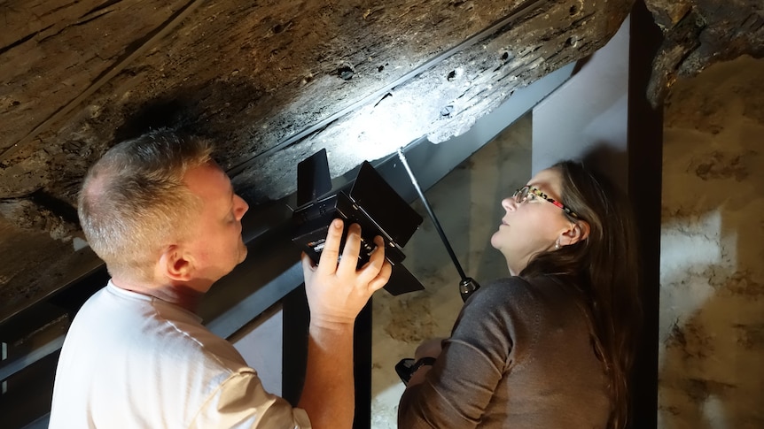 Man shines a light to boat hull as woman holds tool