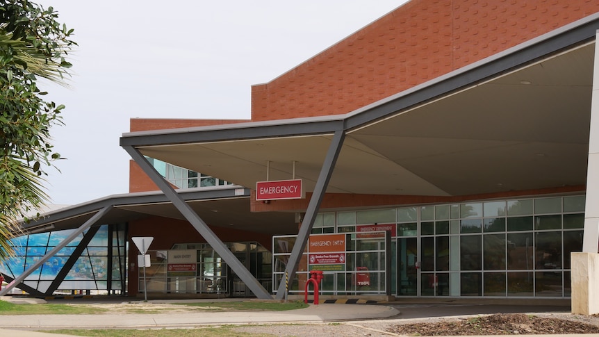 A brown brick building with red signs reading emergency next to a road entrance. The sky is grey.