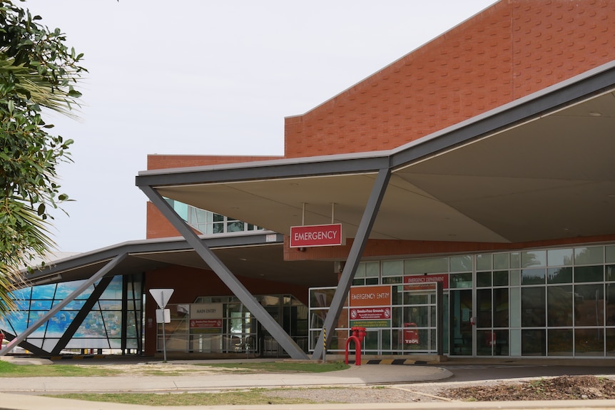 A brown brick building with red signs reading emergency next to a road entrance. The sky is grey.