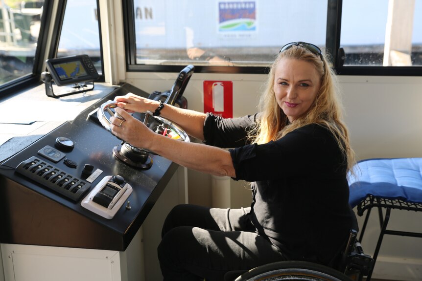 A woman in a wheelchair steering a boat and looking towards the camera