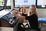 A woman in a wheelchair steering a boat and looking towards the camera