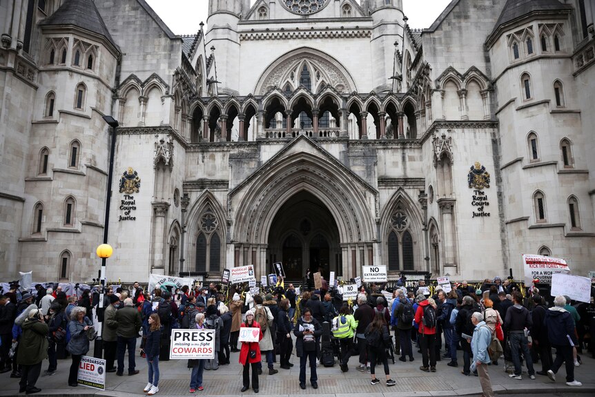 Protesters with signs stand outside London's Royal Courts of Justice.