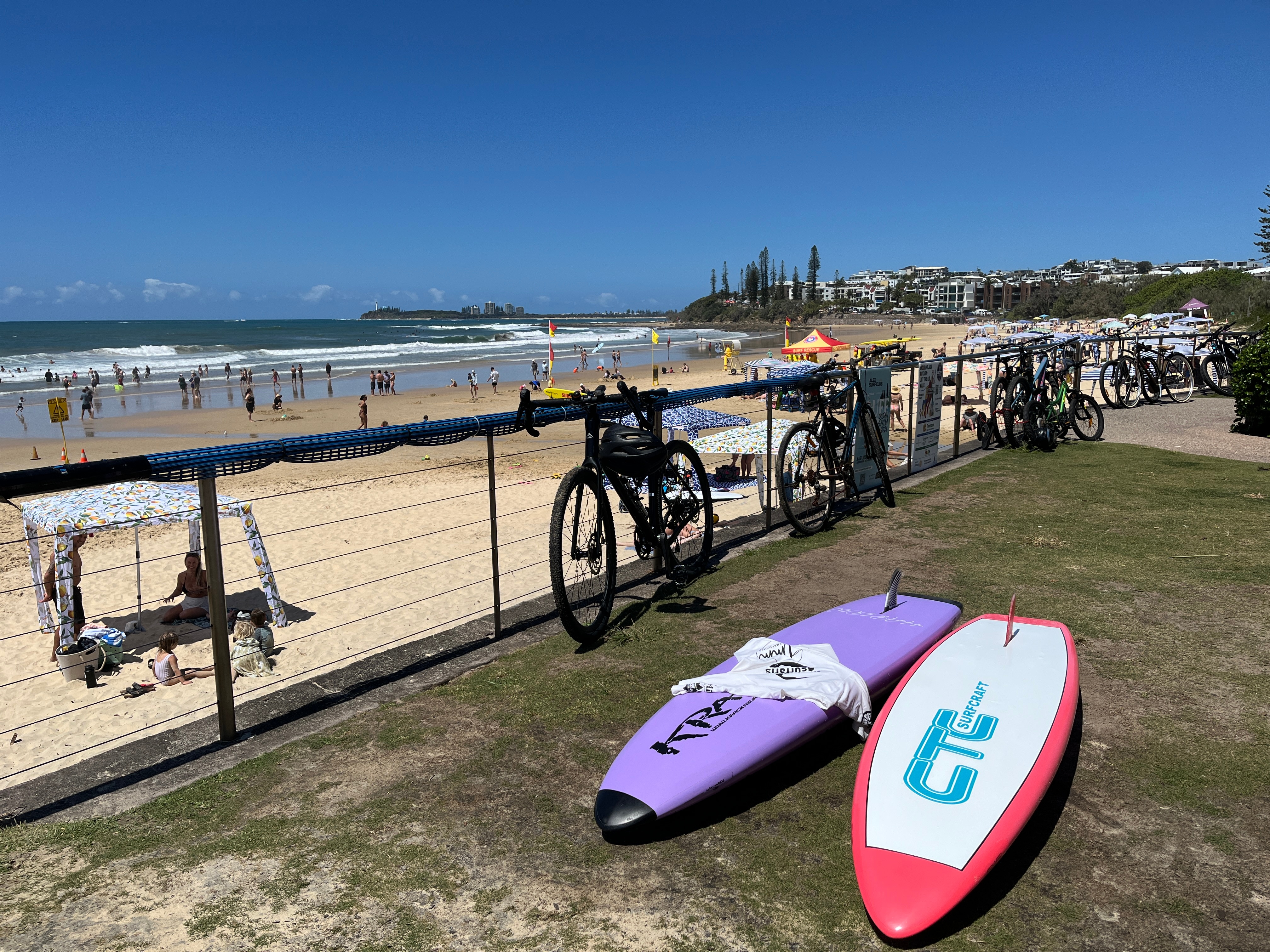 Sunny beach landscape with bikes and surfboards in foreground.