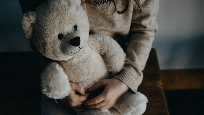 A girl sits on a chair holding a teddy bear.