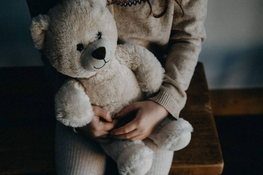 A girl sits on a chair holding a teddy bear.
