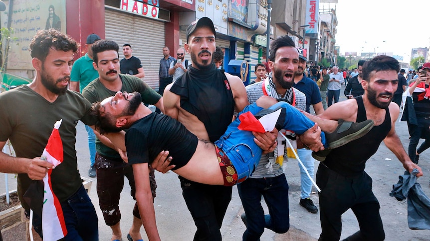 An injured protester is carried in Iraq by fellow protesters as they scream.